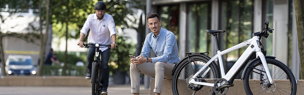 e-Bike Fahrer mit Handy sitzt neben weißem Stromer e-Bike
